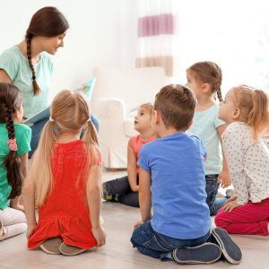 Female teacher reading book to little children in kindergarten