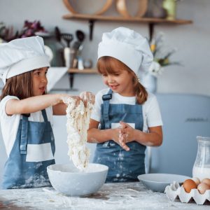 Family kids in white chef uniform preparing food on the kitchen.